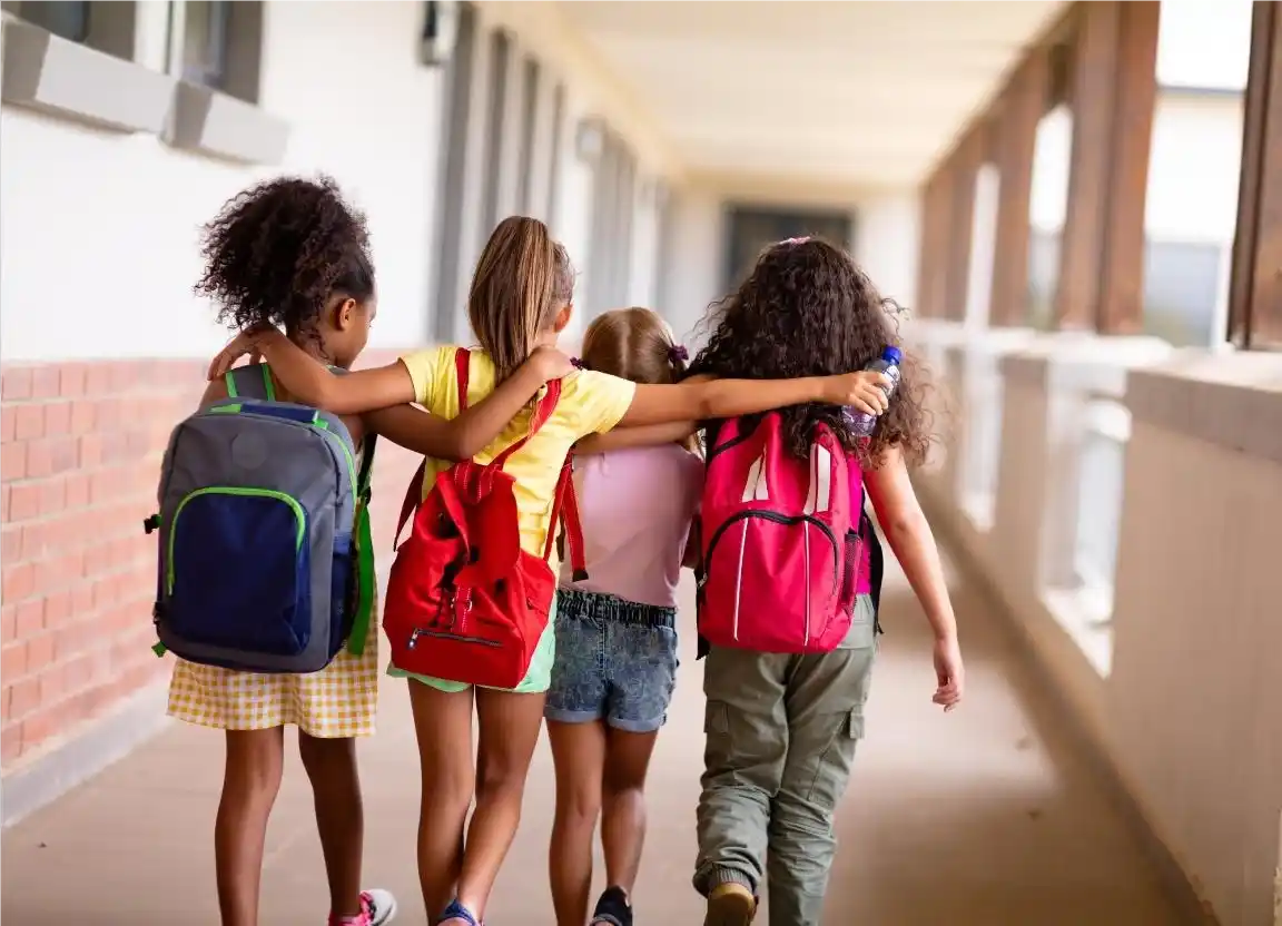 Quatro garotas com mochilas brincando em um corredor